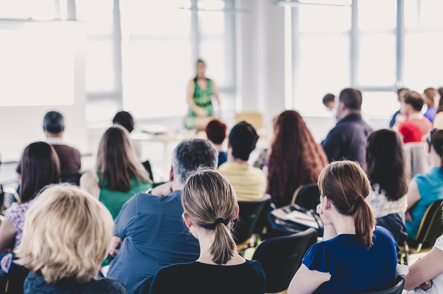 En gruppe mennesker sidder ved borde og ser op mod en underviser